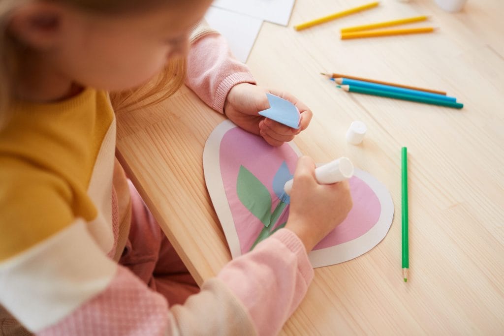 Biglietto decorato con un fiore finto, petali che vengono incollati e colori intorno
