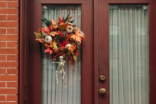 Ghirlanda autunnale con zucche e foglie colorate appesa a una porta, decorata con un piccolo scheletro