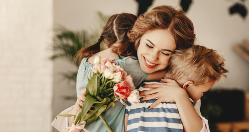 Mamma sorridente abbraccia i suoi figli mentre tiene in mano un bouquet di fiori