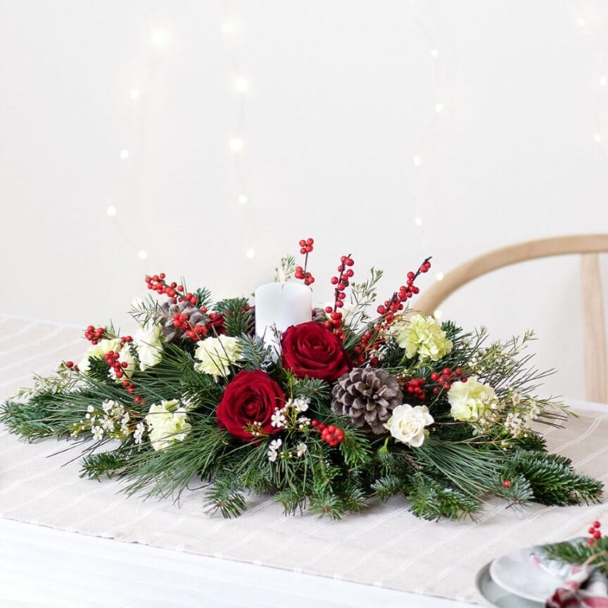 Centrotavola di natale elegante con una candela al centro di un bouquet di fiori con rose rosse, fiori bianchi, pigne e del verde